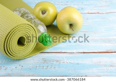 Yoga mat, bottle of water and apples on a wooden background. Equipment for yoga. Concept healthy lifestyle, diet and sport. Copy space. Selective focus
