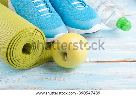 Yoga mat, sport shoes, apple, bottle of water on blue wooden background. Concept healthy lifestyle, healthy food, sport and diet. Sport equipment. Selective focus