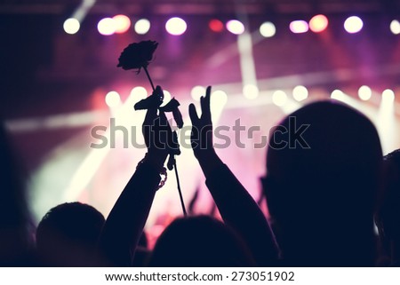 Cheering crowd at a big rock concert. Hands up silhouette with a rose.