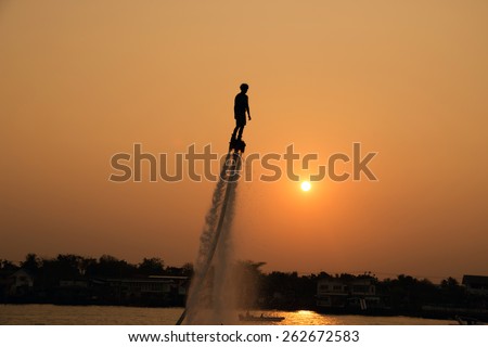 Silhouette of a man showing the fly board in the river of Thailand ; The new spectacular sport
