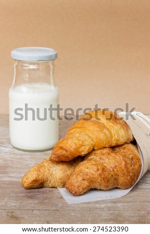 Fresh croissants in a paper wrap with milk from farm on wooden background