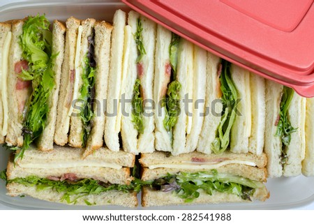 Sandwiches in box for a picnic ; whole wheat and white bread, baby green and red oak leaf lettuce, bacon, cheese and mayonnaise