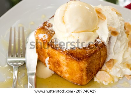 A luscious honey toast with vanilla ice cream on top ; whipped cream and almond slice