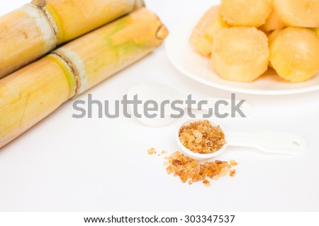 Brown sugar and refined sugar in measuring spoon with sugar cane background