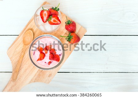 Fresh juicy strawberry with yogurt in a glass bowl and fresh strawberry on ice serving wood platter ; top view