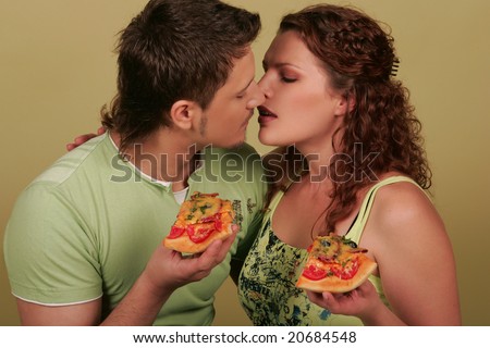 Young man and young woman kissing with pizza in their hands