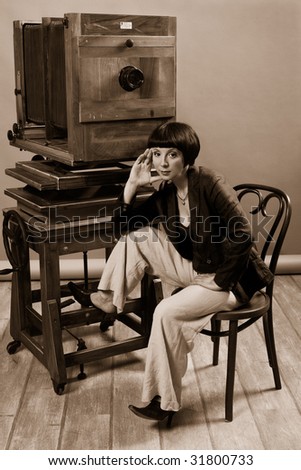 Young woman sit near the old vintage camera in photographic studio