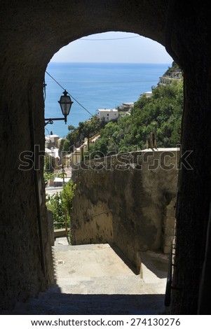 An arch of the pedestrian walkway make a window onto the steep slopes of Positano, Campania, Italy, along the Amalfi Coast. The Mediterranean Sea is in the background.