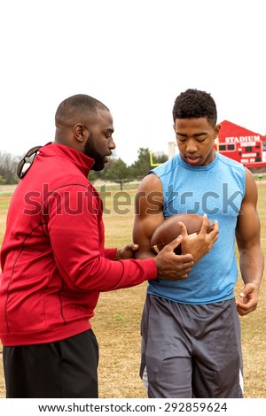 Football coach coaching a football player on the football field.