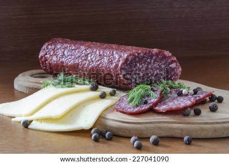 stick sausage lies on a wooden board cut pieces of cheese spice pepper and greens