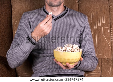 Young guy watching TV on the couch and eating popcorn