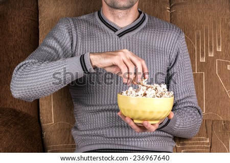 Young guy watching TV on the couch and eating popcorn
