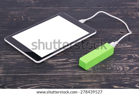 Tablet PC charged by the mobile charger on a wooden dark background