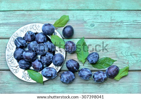 Blue plums on metal plate and wooden background. top view