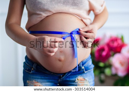 A pregnant woman close up with a blue ribbon tied on the tummy