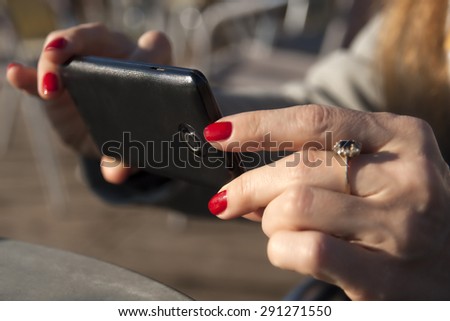 Two feminine hands with red nail polish holding a mobile phone
