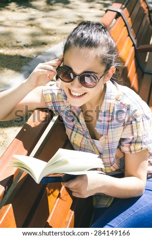 Young beautiful woman smiling reading a book sitting on a bench