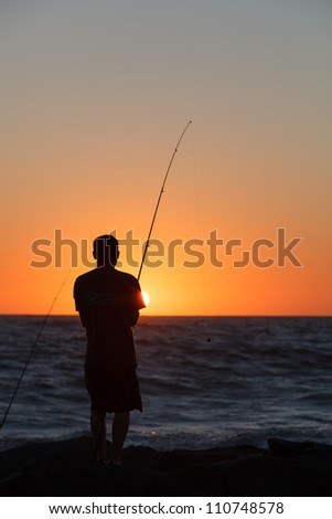 Person fishing on rocks at sunset