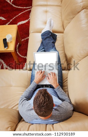 Man stretched out on sofa using a modern laptop - Clipping path for laptop screen