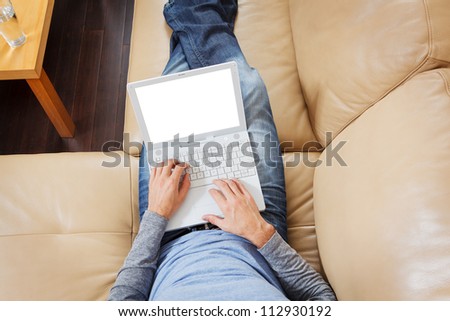 Closeup of Man stretched out on sofa using a modern laptop - Clipping path for laptop screen