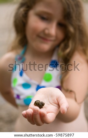 happy little girl holding snail shell in palm of hand, focus on shell