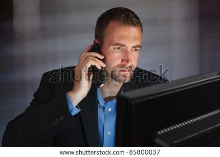 Photo of a concerned young businessman working at his computer while talking on the phone. Looking at computer monitor