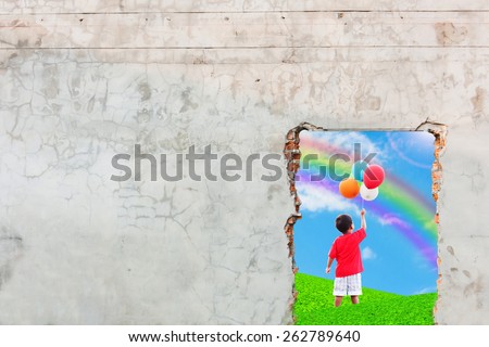 the boy standing on the green grass and hand hold bubble looking at rainbow on blue sky old brick wall background