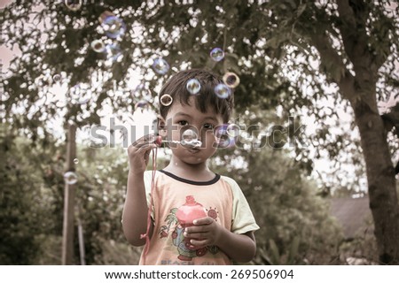 Little boy playing with bubble wand blowing soap bubbles,vintage tone