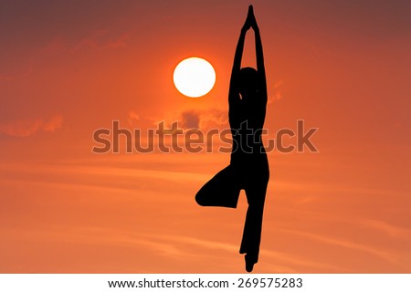 Silhouette young woman practicing yoga on the sky orange sunset.