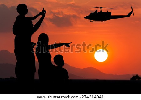 Parents and children look at the helicopter on the sky at sunset