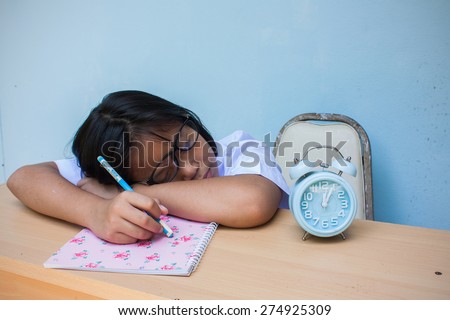 asian girl child student sleeping on the table with books and clock over blue background