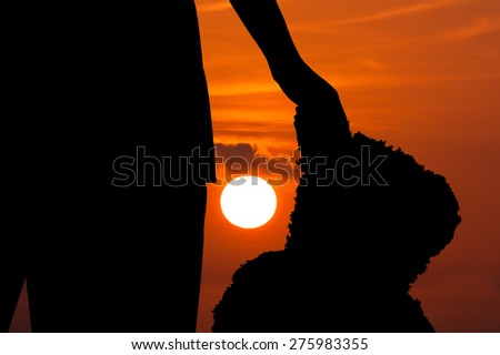 silhouette of girl standing alone and hand hold mini bear at sunset background