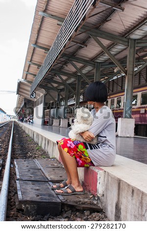 sad girl  sitting alone on a bench with teddy bear looking at railway waiting someone