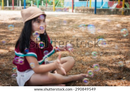 blurry abstract of little asian cute girl  playing with bubble wand blowing soap bubbles in the garden background