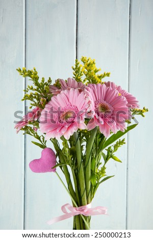 Bouquet of pink gerbera flowers  and a toy heart for Valentine\'s day on light blue wooden background.