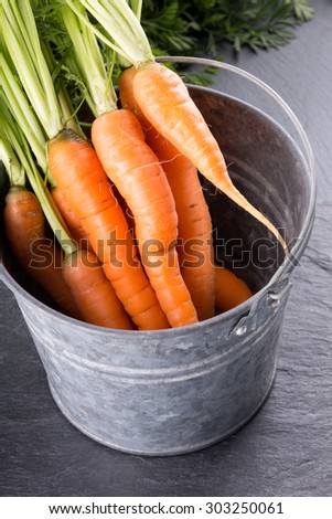 A bunch of fresh carrots in tin bucket on black slate background.