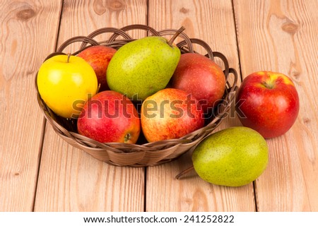 Apples and pears in the basket on the wooden background.
