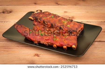 Grilled meat ribs on the black plate on the wooden background.