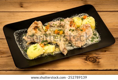 Rabbit cooked in sour cream with vegetables on the black plate on the wooden background.