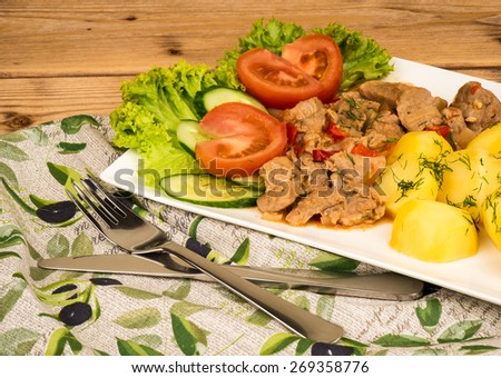 Stewed meat with potatoes on the wooden background.