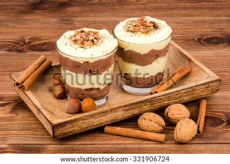 Sweet dessert - chocolate and vanilla pudding in glasses served on the wooden tray with nuts and  cinnamon sticks.