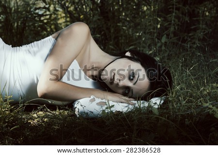 Pale woman in white dress lying on the ground, fairytale scene