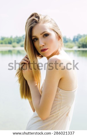 Sexy blonde girl on the lake shore, holding hair in hands
