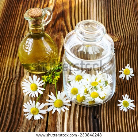 the picked camomile flowers in a glass jar on a brown wooden background