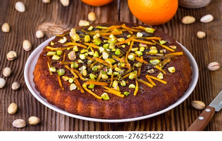 sweet pie with pistachios and a dried peel of orange on a round wooden board on a brown wooden background