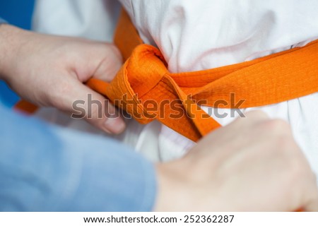 A father ties an orange belt on his son\'s uniform for martial arts