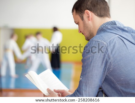 Father reading a book while waiting for his kids training martial arts