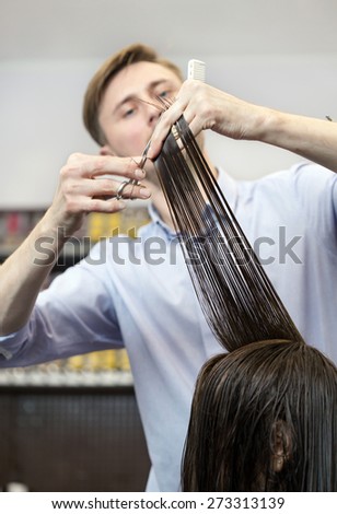 Handsome hairdresser making a haircut for a brunette girl
