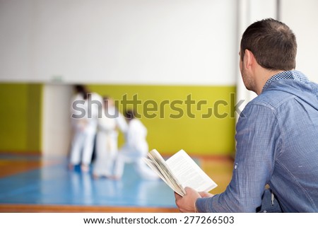 Father reading a book while waiting for his kids training martial arts