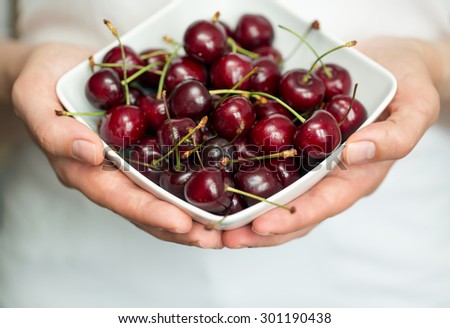 Female hands holding a white bowl with ripe cherries. Shallow dof